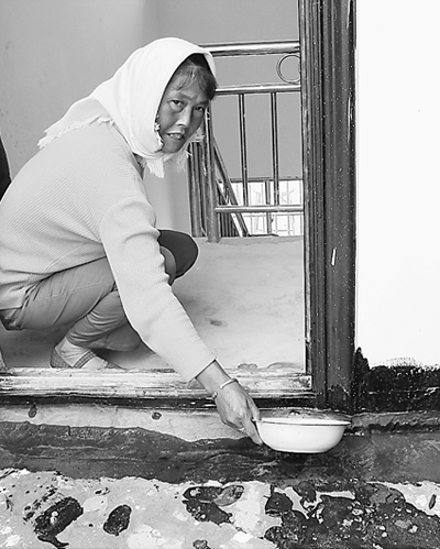 村民李菊花在舀漏在新居里的雨水。